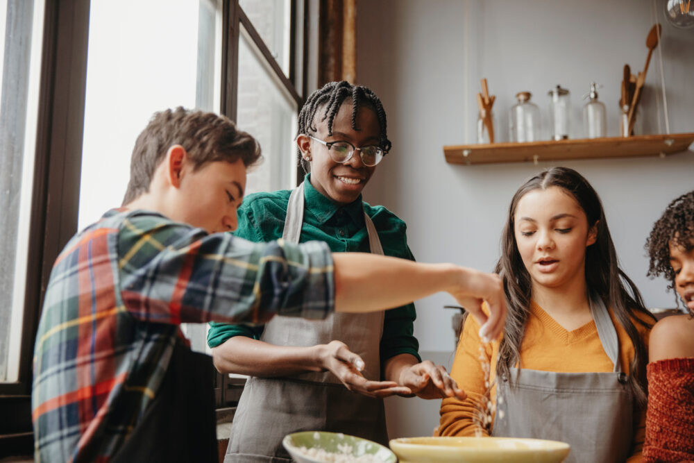 Students preparing food while standing against wall in kitchen